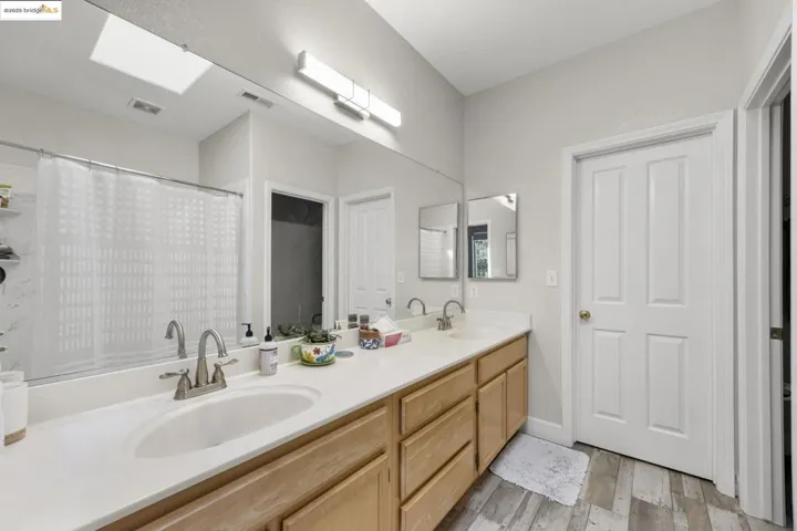 Full bath featuring double vanity, light wood-style floors, a skylight, and curtained shower
