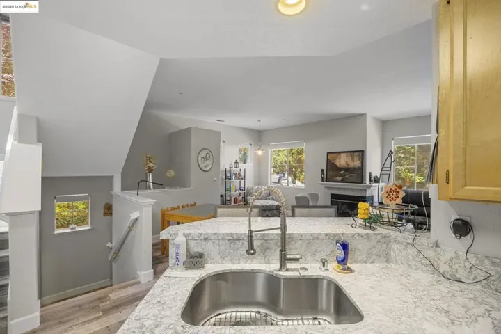 Kitchen with healthy amount of natural light, light wood finished floors, light stone countertops, a fireplace, and vaulted ceiling