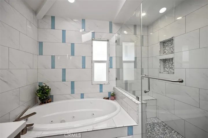 Over-sized walk in shower with two Kohler shower heads, stone floor and bench