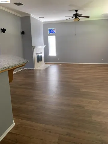 Unfurnished living room with ornamental molding, ceiling fan, dark wood finished floors, and a tiled fireplace