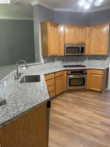Kitchen with light stone countertops, crown molding, appliances with stainless steel finishes, light wood-type flooring, and backsplash