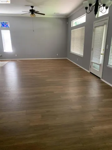 Unfurnished living room featuring ornamental molding, a chandelier, a ceiling fan, and dark wood-type flooring