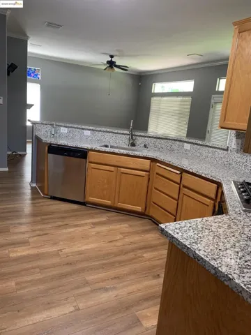 Kitchen with light stone counters, appliances with stainless steel finishes, ceiling fan, light wood-style flooring, and crown molding