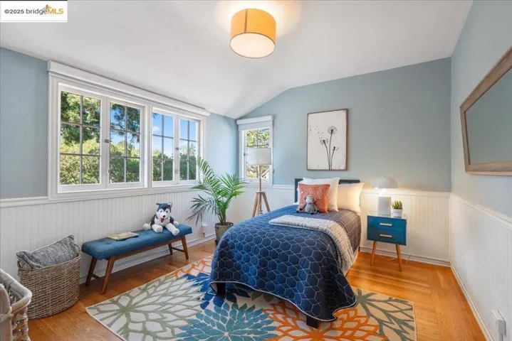 Bedroom featuring wainscoting, wood finished floors, and lofted ceiling