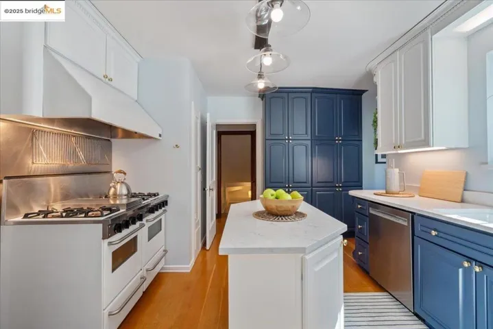 Kitchen featuring blue cabinets, white cabinetry, light wood finished floors, range with two ovens, and a center island