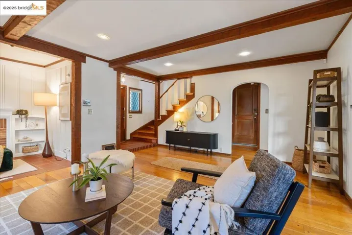 Living room with beam ceiling, arched walkways, hardwood / wood-style flooring, crown molding, and stairs