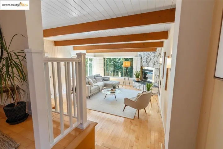 Living area with wood-type flooring, a stone fireplace, and beam ceiling