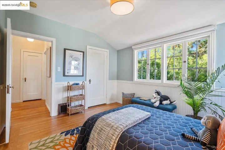 Bedroom featuring wood finished floors, vaulted ceiling, and wainscoting