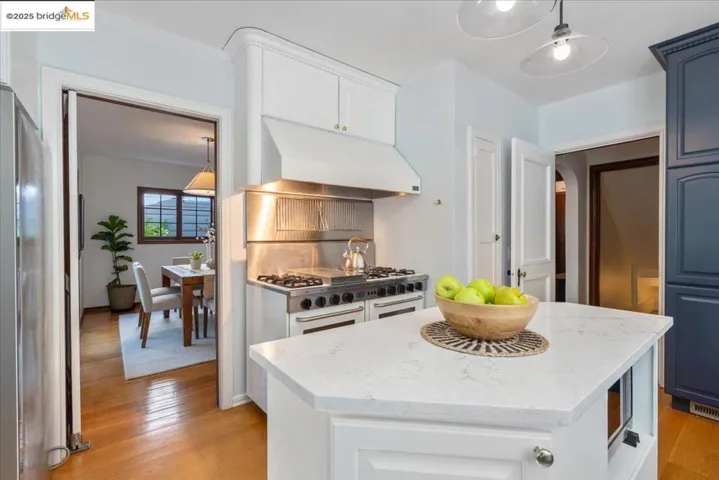 Kitchen with hanging light fixtures, light wood-style flooring, light stone countertops, under cabinet range hood, and a kitchen island