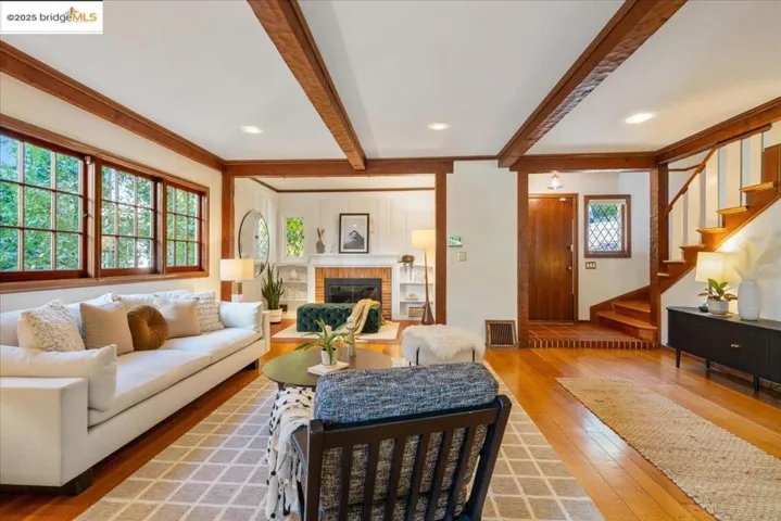 Living room with beam ceiling, light wood-type flooring, stairway, a fireplace, and ornamental molding