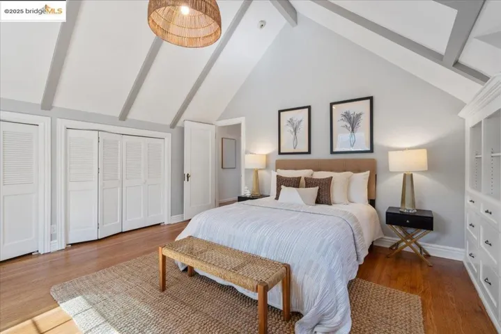 Bedroom with beam ceiling, multiple closets, high vaulted ceiling, and wood finished floors