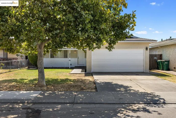 View of property hidden behind natural elements with concrete driveway, stucco siding, an attached garage, brick siding, and a porch