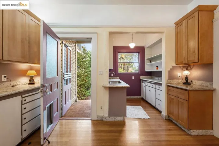 Kitchen with light stone counters, brown cabinetry, light wood finished floors, decorative light fixtures, and open shelves