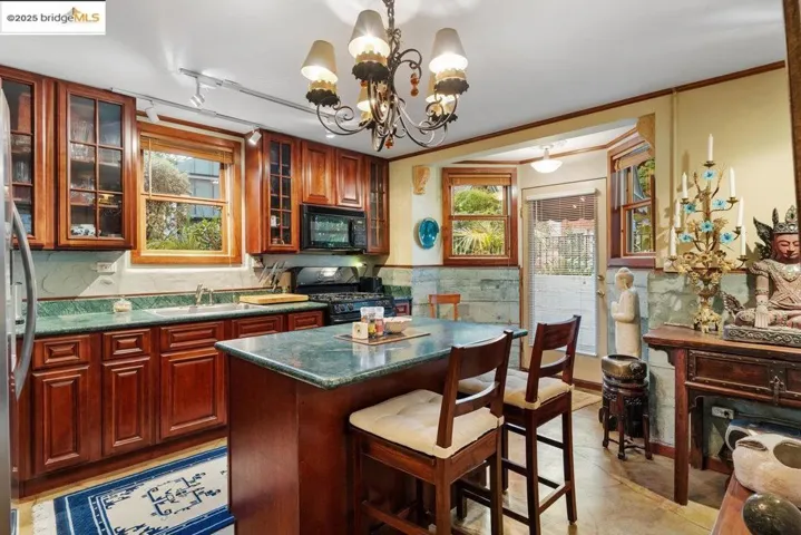 Kitchen featuring a kitchen island, a breakfast bar area, decorative light fixtures, a wainscoted wall, and black appliances