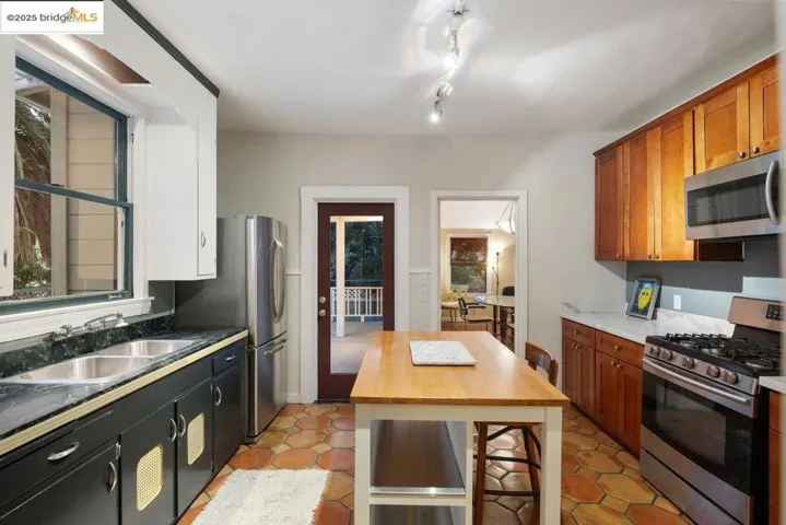Kitchen featuring appliances with stainless steel finishes, light tile patterned flooring, and brown cabinetry