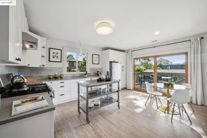 Kitchen with white cabinets, decorative backsplash, stainless steel appliances, under cabinet range hood, and pendant lighting