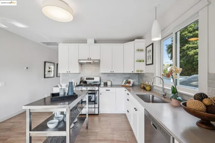 Kitchen featuring decorative light fixtures, appliances with stainless steel finishes, decorative backsplash, white cabinets, and light wood-style floors