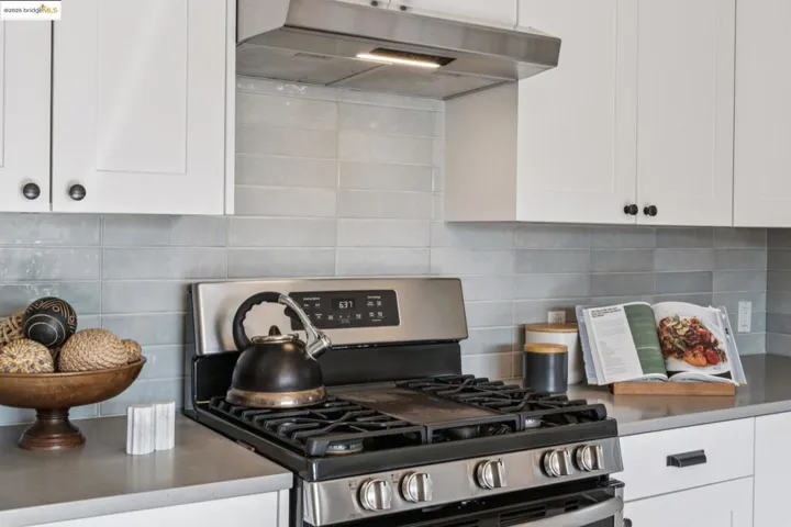 Kitchen featuring stainless steel range with gas cooktop, white cabinets, backsplash, and under cabinet range hood