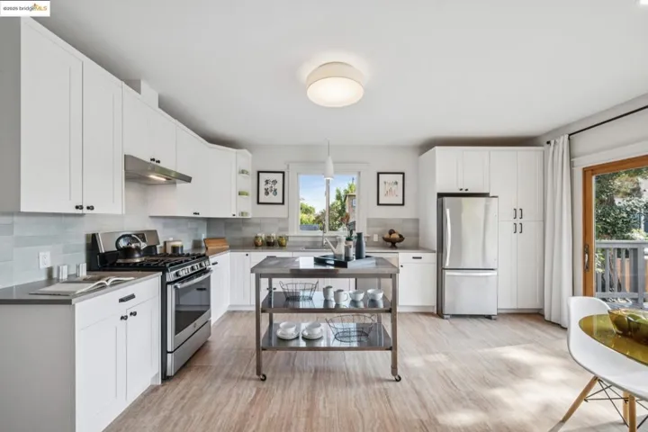 Kitchen with stainless steel appliances, white cabinets, backsplash, under cabinet range hood, and dark countertops