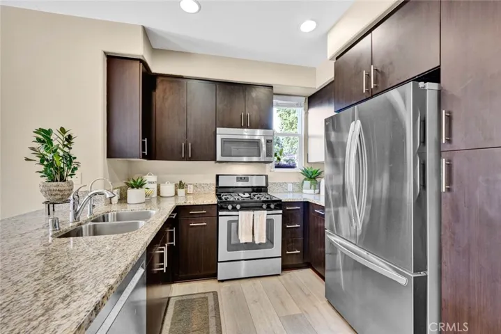 Kitchen has rich dark wood cabinetry, stainless appliances, stainless sinks, and granite countertops
