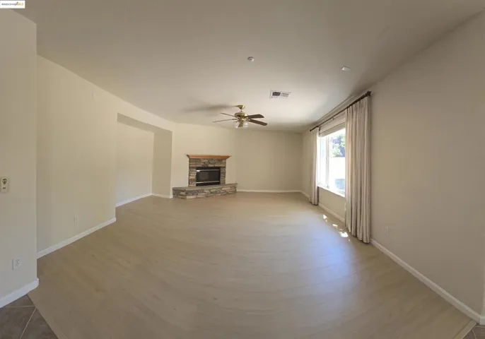 Unfurnished living room featuring a stone fireplace, light wood-type flooring, and ceiling fan