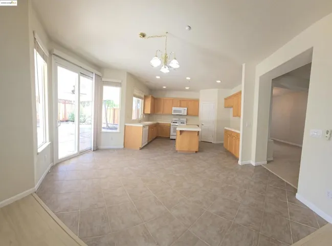 Kitchen with light countertops, a chandelier, light brown cabinetry, white appliances, and a kitchen island