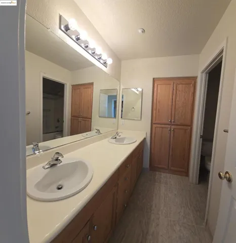 Bathroom featuring double vanity, a textured ceiling, and dark tile patterned floors