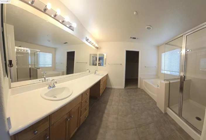 Full bathroom with a garden tub, a stall shower, double vanity, and dark tile patterned floors