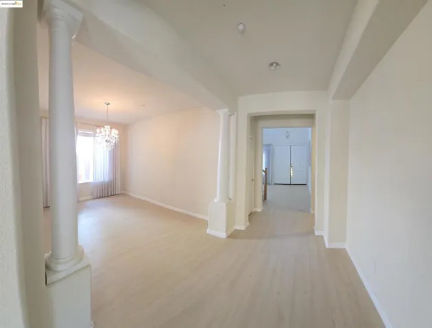 Hallway featuring light wood finished floors, ornate columns, and a chandelier
