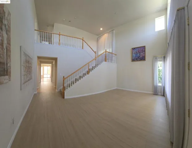 Unfurnished living room with a high ceiling, light wood-style flooring, stairway, plenty of natural light, and recessed lighting