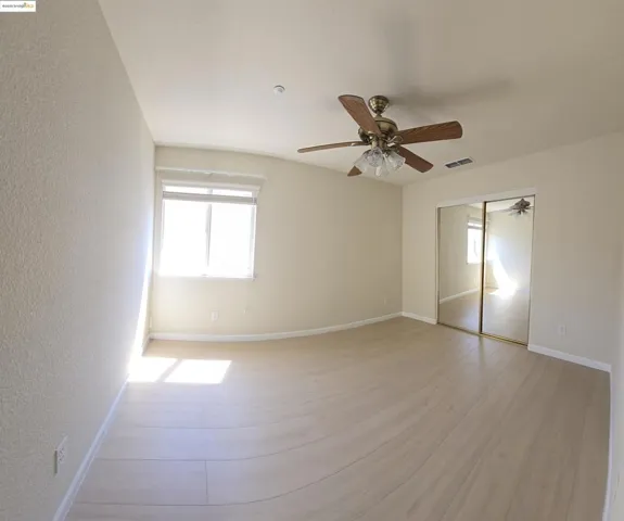Unfurnished bedroom featuring a textured wall, light wood-style floors, a closet, and a ceiling fan