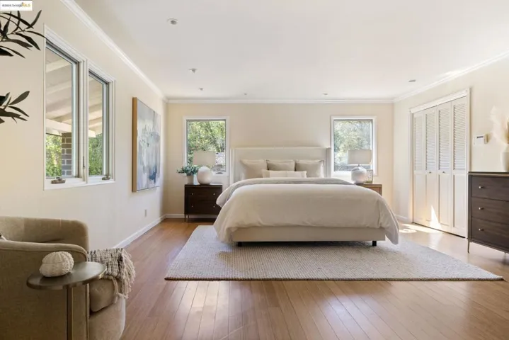 Bedroom with wood-type flooring, crown molding, multiple windows, and a closet