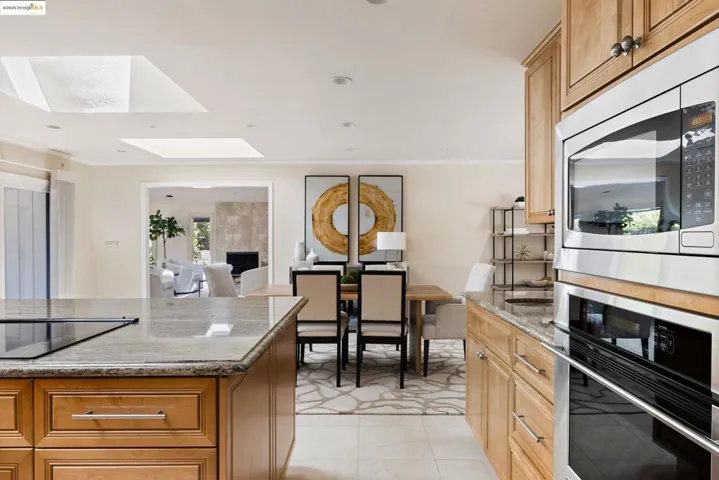 Kitchen featuring dark stone counters, appliances with stainless steel finishes, a skylight, ornamental molding, and a tiled fireplace