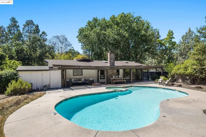 View of swimming pool with a patio area, a pool with connected hot tub, and view of wooded area