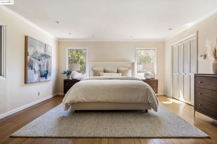 Bedroom with wood finished floors, ornamental molding, multiple windows, and a closet