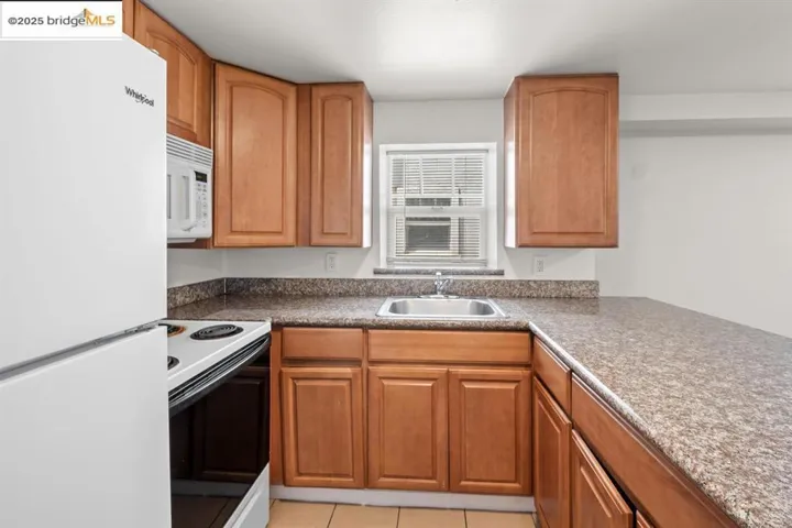 Kitchen with white appliances, light tile patterned floors, brown cabinets, and dark countertops