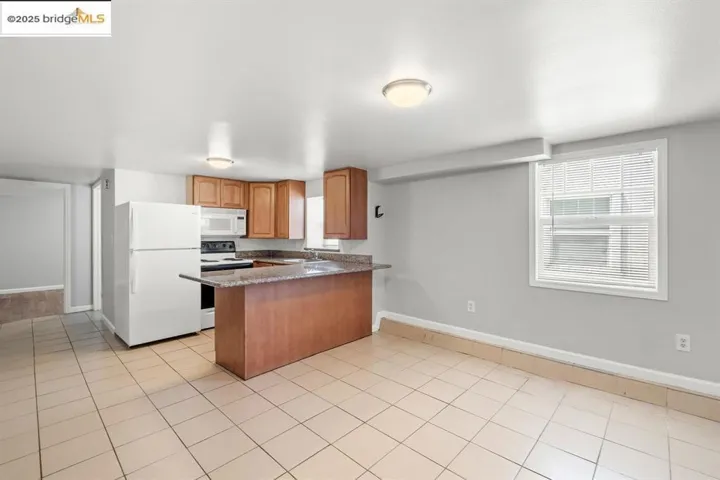 Kitchen featuring white appliances, plenty of natural light, a peninsula, and light tile patterned flooring
