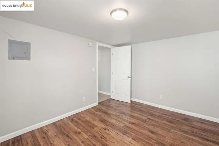 Spare room with electric panel and dark wood-style flooring