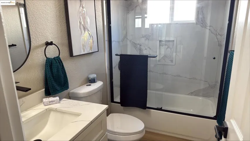 Bathroom featuring a textured wall, enclosed tub / shower combo, and vanity
