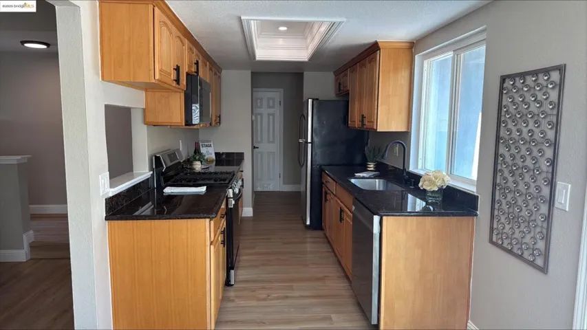 Kitchen with appliances with stainless steel finishes, light wood-type flooring, dark stone counters, a textured ceiling, and a raised ceiling