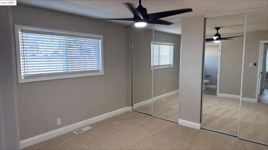 Unfurnished bedroom with light carpet, two closets, and ceiling fan