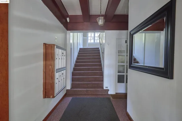 Stairs with beamed ceiling, mail area, and carpet flooring