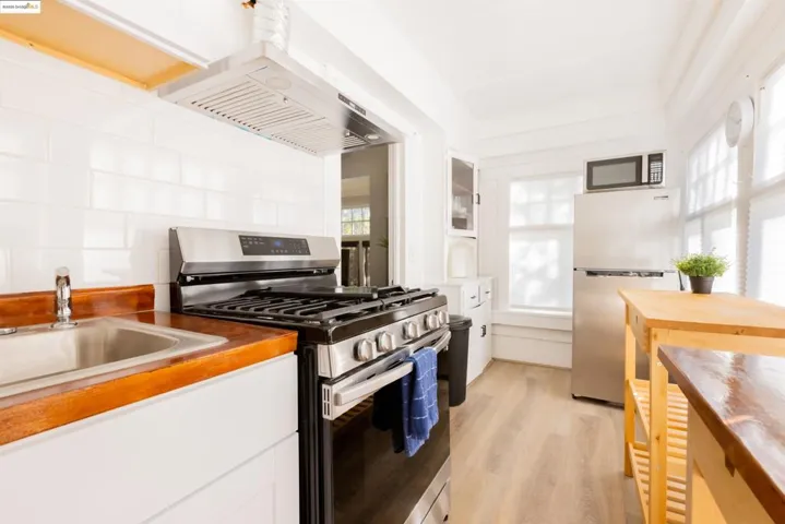 Kitchen featuring stainless steel appliances, white cabinets, light wood-type flooring, island range hood, and backsplash