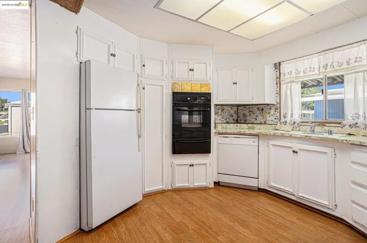 Kitchen featuring plenty of natural light, white cabinets, white appliances, and light wood-style flooring