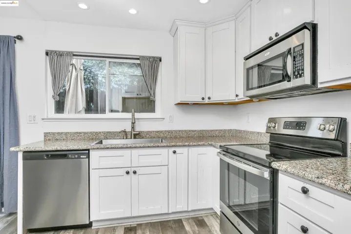 Kitchen with appliances with stainless steel finishes, white cabinets, light stone countertops, light wood finished floors, and recessed lighting