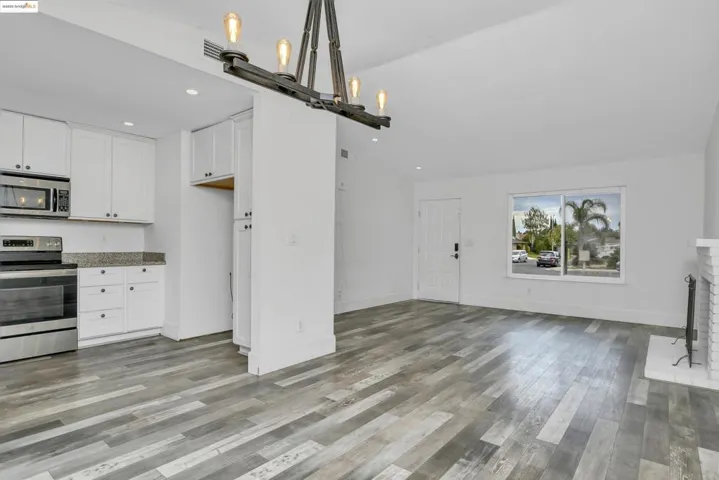 Kitchen with stainless steel appliances, white cabinets, vaulted ceiling, light stone counters, and a brick fireplace