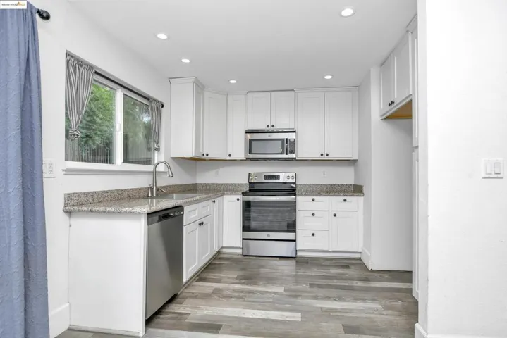 Kitchen featuring appliances with stainless steel finishes, white cabinets, light stone countertops, recessed lighting, and light wood-style flooring