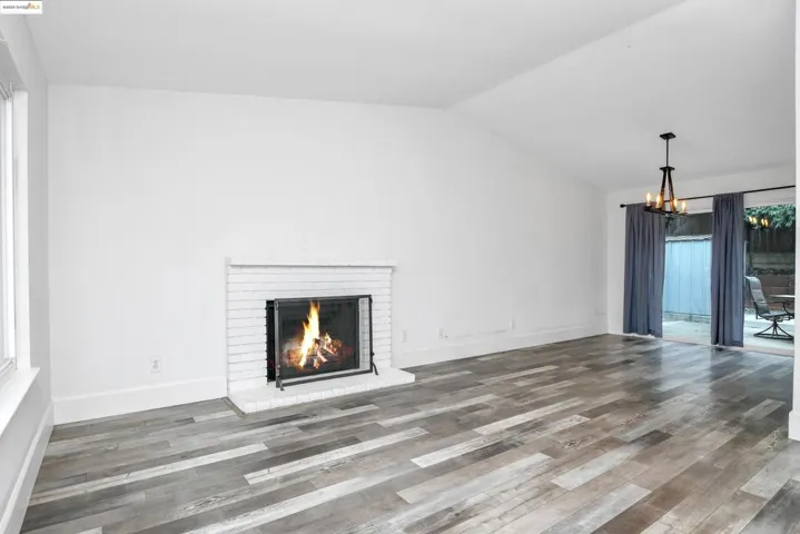 Unfurnished living room with a fireplace, lofted ceiling, wood finished floors, and a chandelier