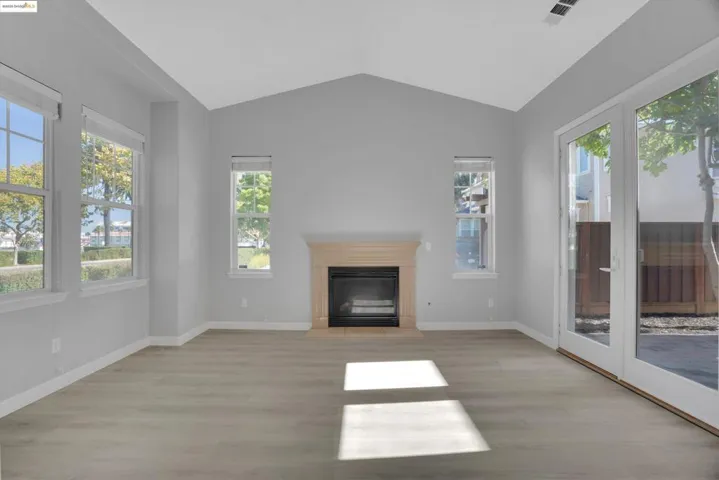 Unfurnished living room featuring light wood-type flooring, a glass covered fireplace, and lofted ceiling