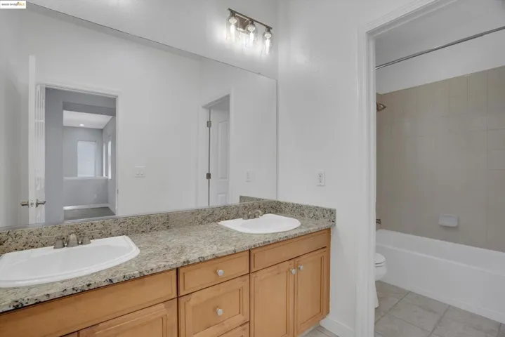 Bathroom featuring washtub / shower combination, double vanity, and light tile patterned floors